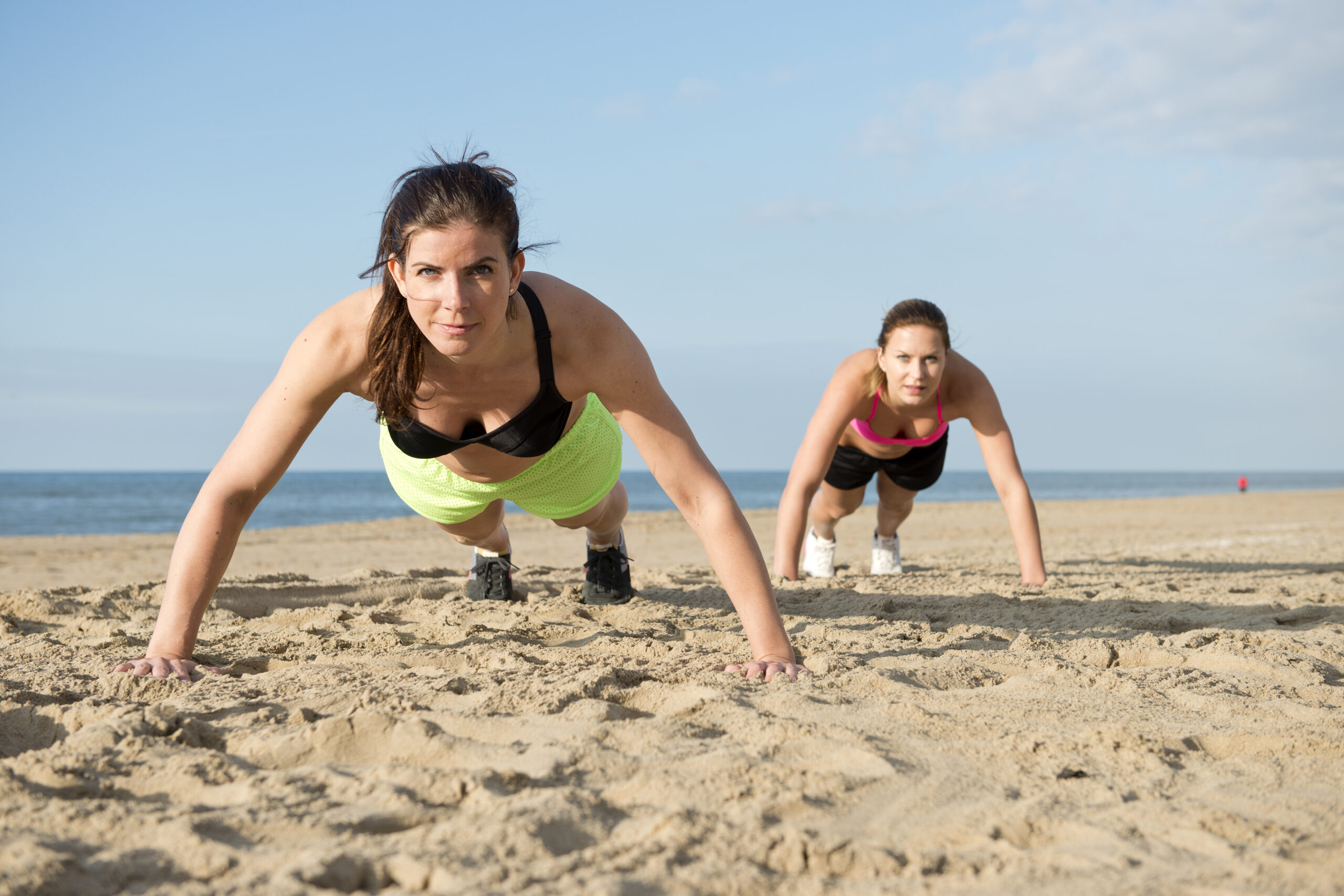 Two,Women,Doing,Pushups,On,A,Beach,During,An,Intense Fitness